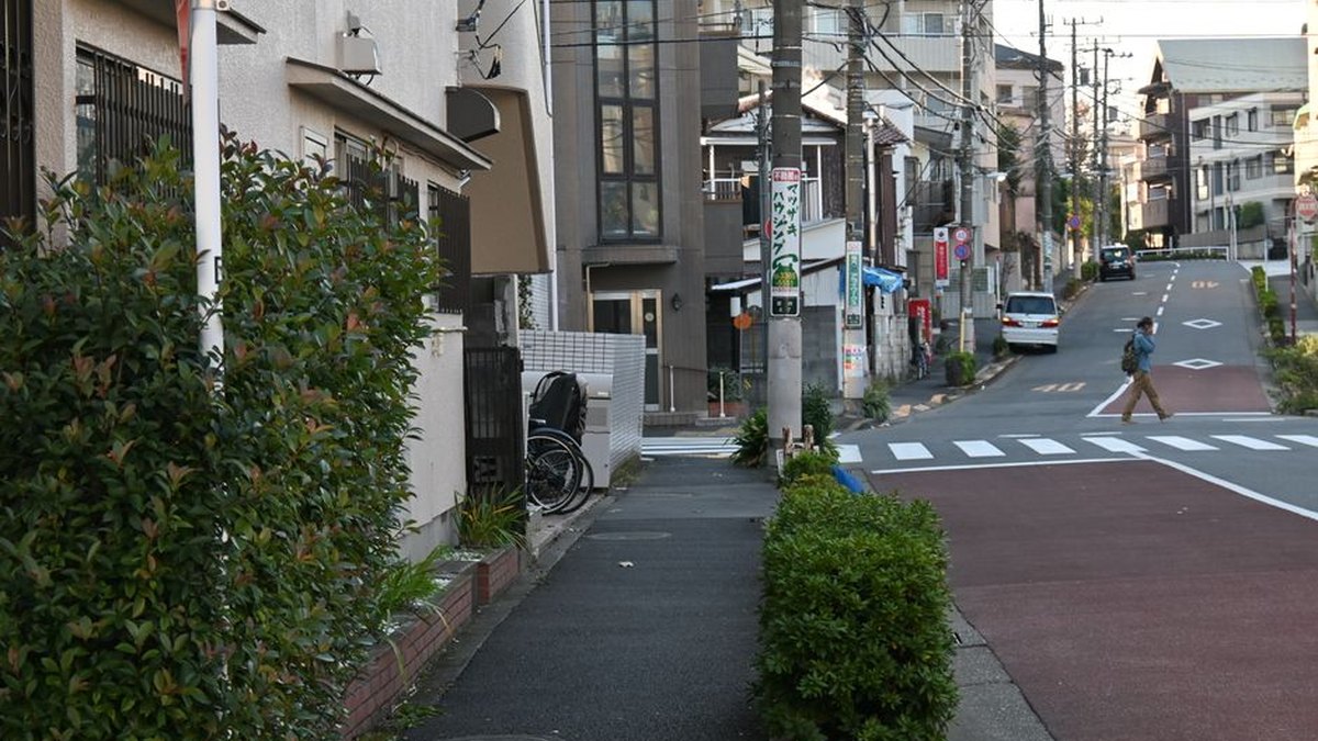 A peaceful urban street in Japan with a lone pedestrian crossing and residential buildings.